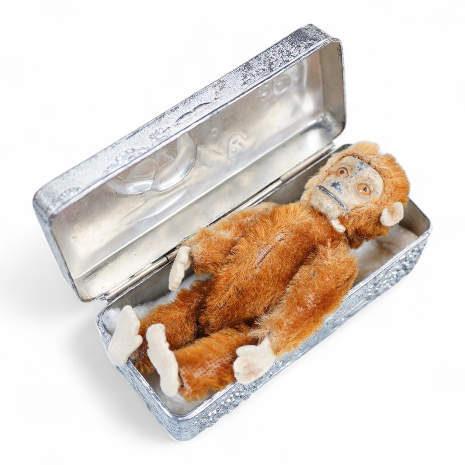A German Schuco scent bottle monkey, with mohair body containing a glass bottle, together with a white metal Japanese style lid box decorated with a floral landscape and bird of prey to the lid
